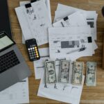 Overhead view of financial documents, cash, and technology on a wooden desk.