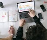 Two people collaborating on a laptop and planner at a vibrant modern office desk.